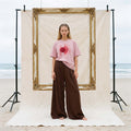 AYLA boxy vintage washed tee in blush organic cotton, worn with brown wide-leg trousers on a Byron Bay beach set – Oldest Daughter