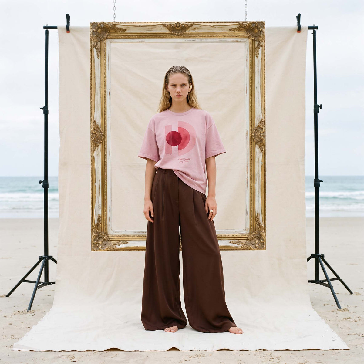 AYLA boxy vintage washed tee in blush organic cotton, worn with brown wide-leg trousers on a Byron Bay beach set – Oldest Daughter