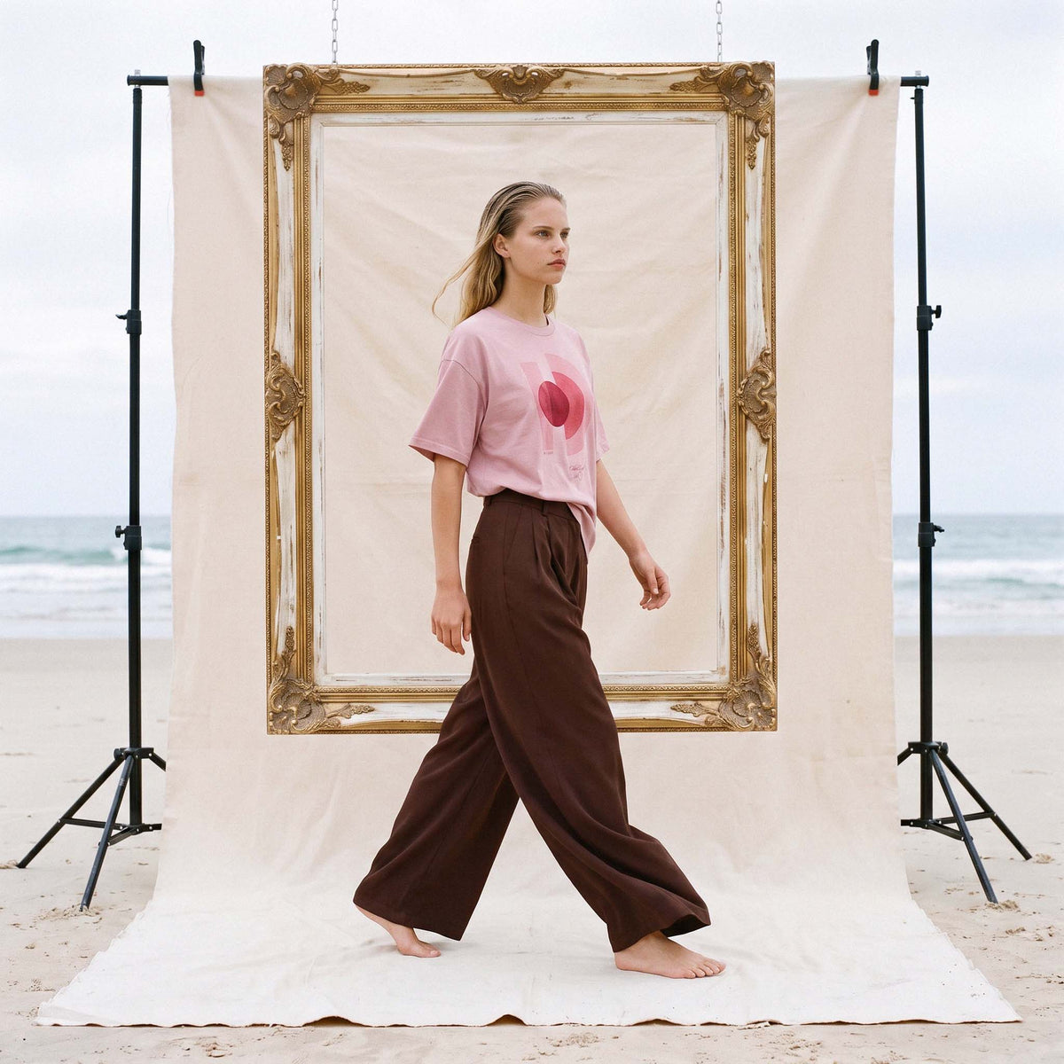 Model walking barefoot in the AYLA blush organic cotton tee and wide-leg trousers – Oldest Daughter, Byron Bay