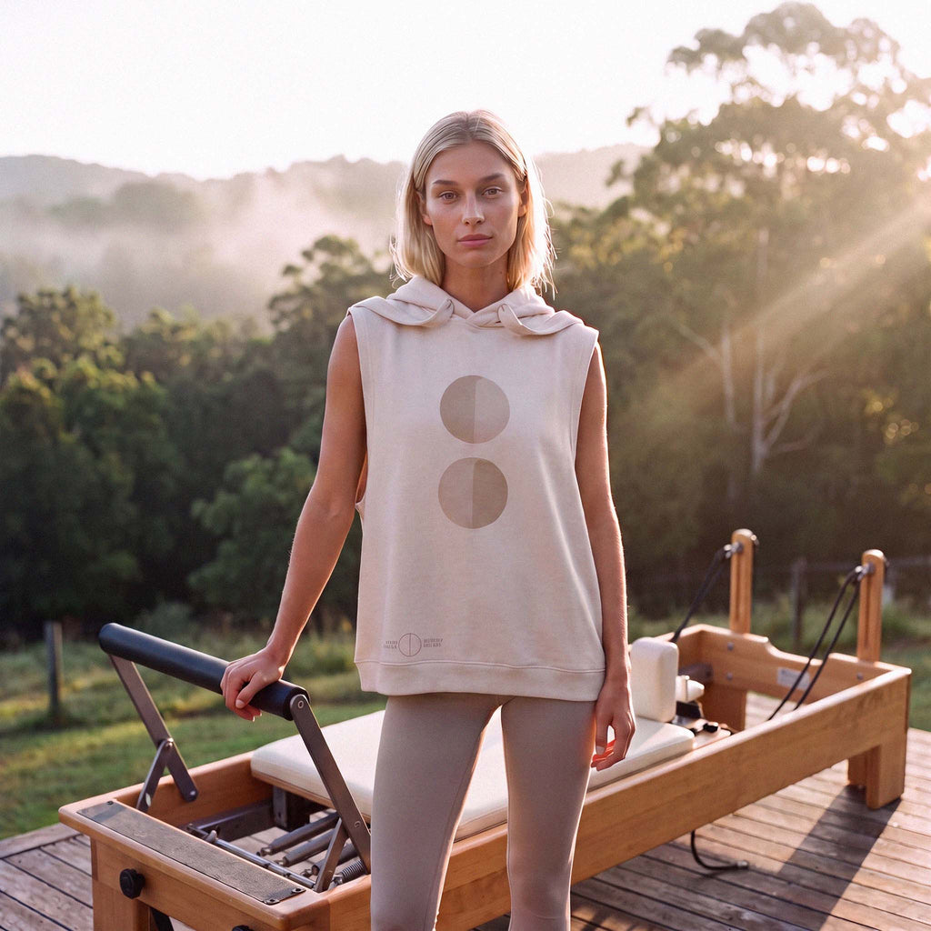 Model wearing the INES organic cotton sleeveless hooded tank on a pilates reformer – Oldest Daughter, Byron Bay